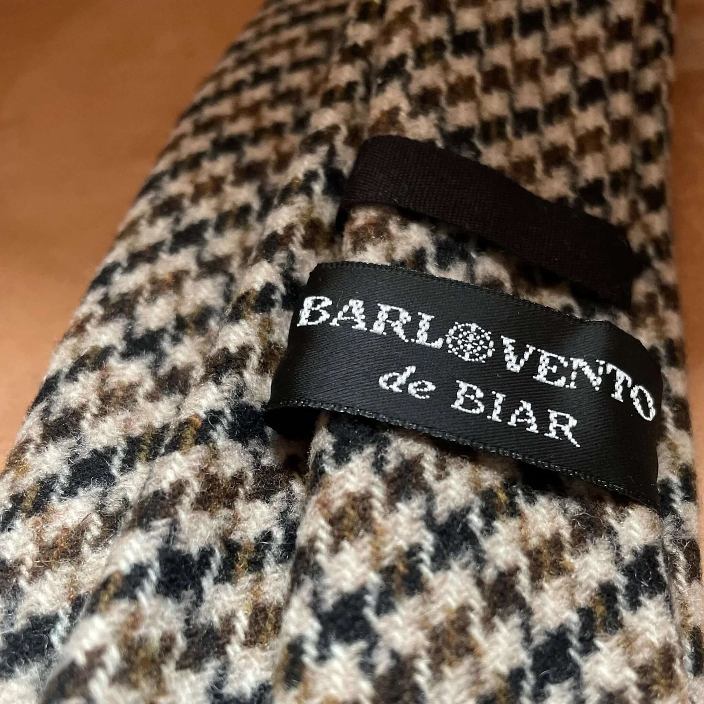 Corbata de lana con patrón de pata de gallo en tonos marrón, negro y crema. Textura suave y clásica.