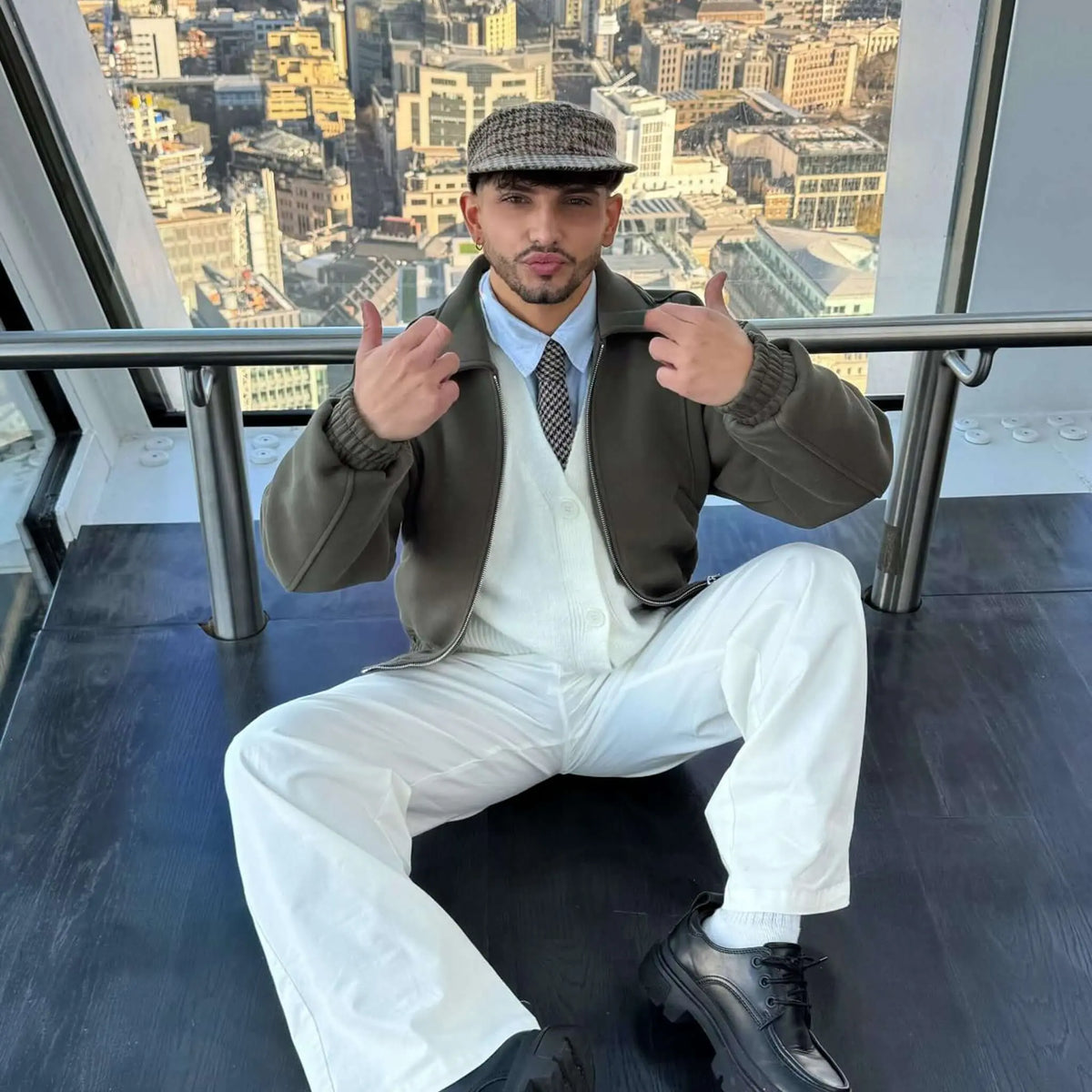 Hombre con corbata de lana con patrón pata de gallo, chaqueta verde, cárdigan blanco y boina a juego. Vista urbana.