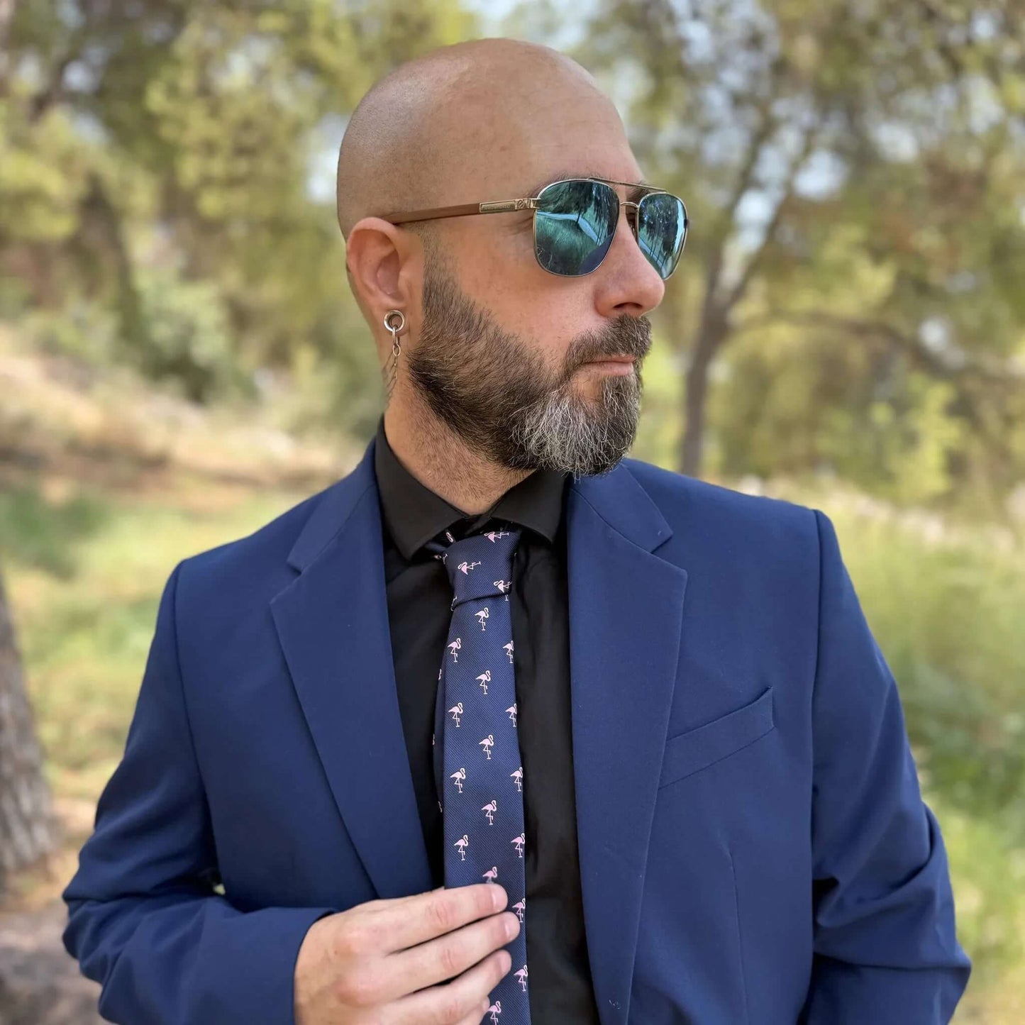 Corbata azul marino delgada con estampado de pequeños flamencos rosas, sobre camisa negra y traje azul.