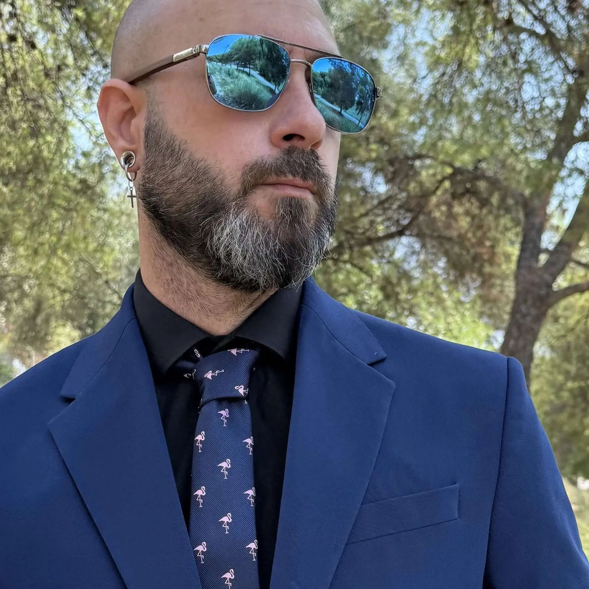 Hombre con americana azul, camisa negra y corbata azul marino estampada con pequeños flamencos rosas.