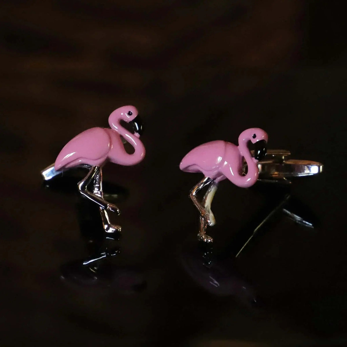 Gemelos de diseño moderno con forma de flamenco rosa, acabado esmaltado brillante y estructura metálica plateada.