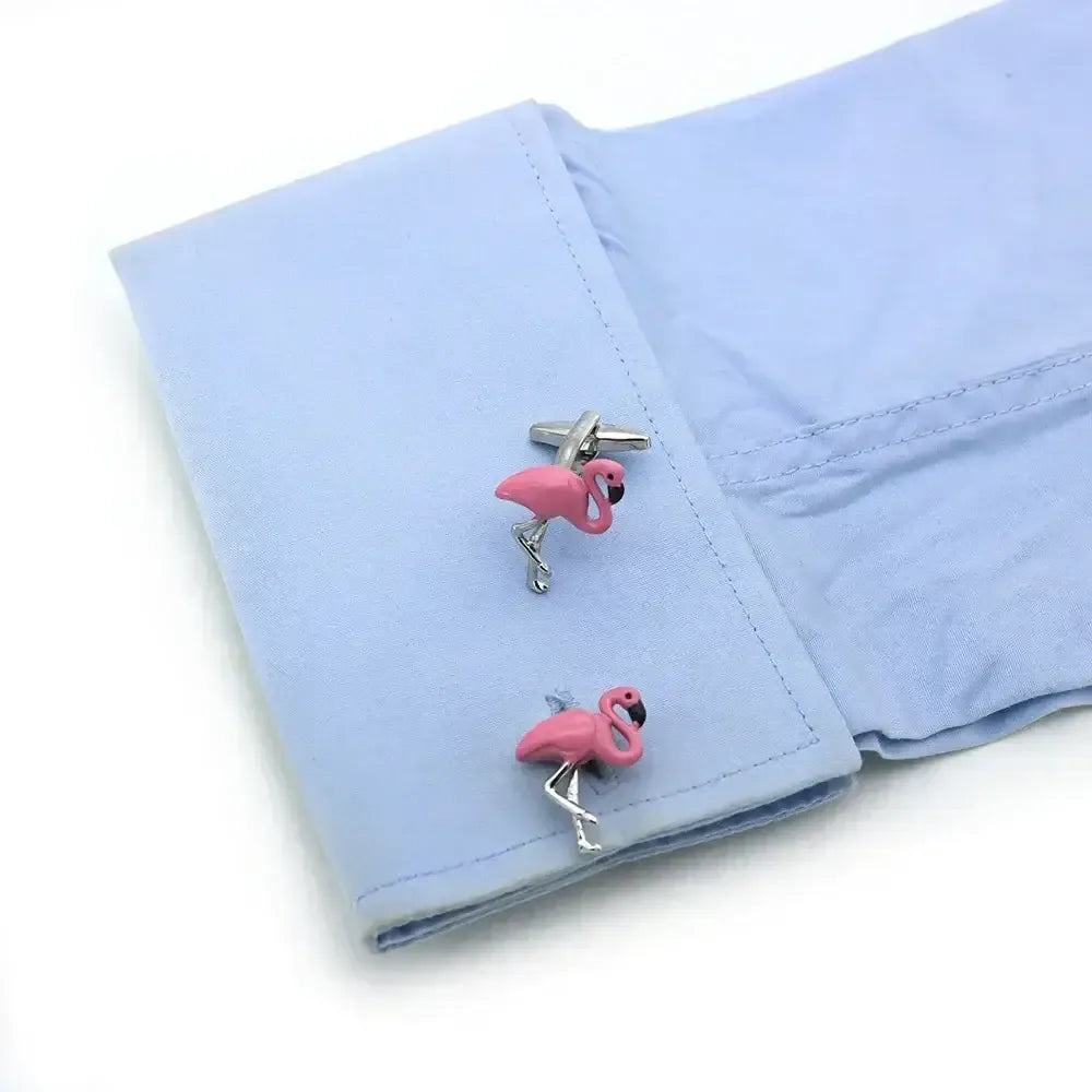 Gemelos de metal plateado con forma de flamenco rosa esmaltado colocados en el puño de una camisa azul claro.