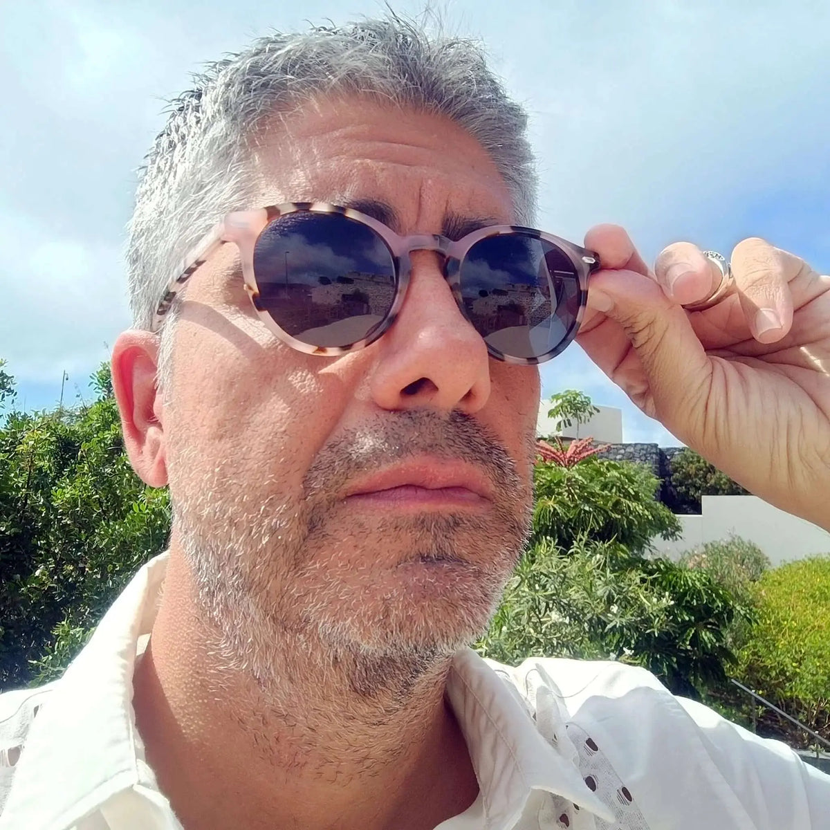 Hombre con gafas de sol redondas de acrílico con patrón carey y montura mate, estilo casual en un entorno soleado.