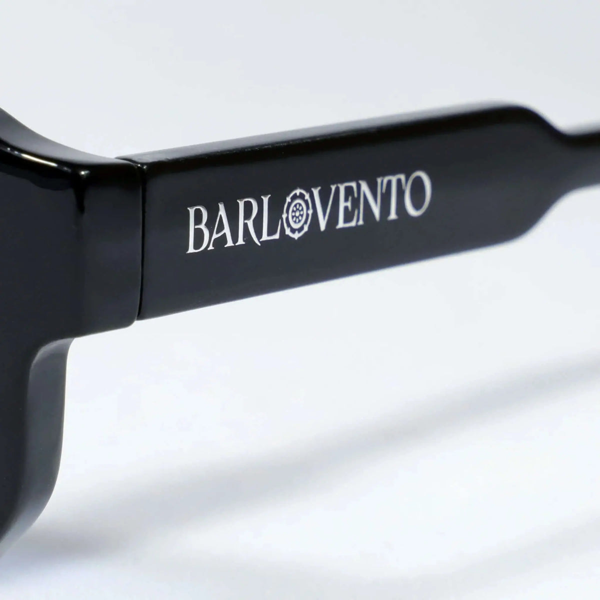 Detalle lateral de una patilla de gafas de sol de acetato negro brillante con grabado en color blanco.