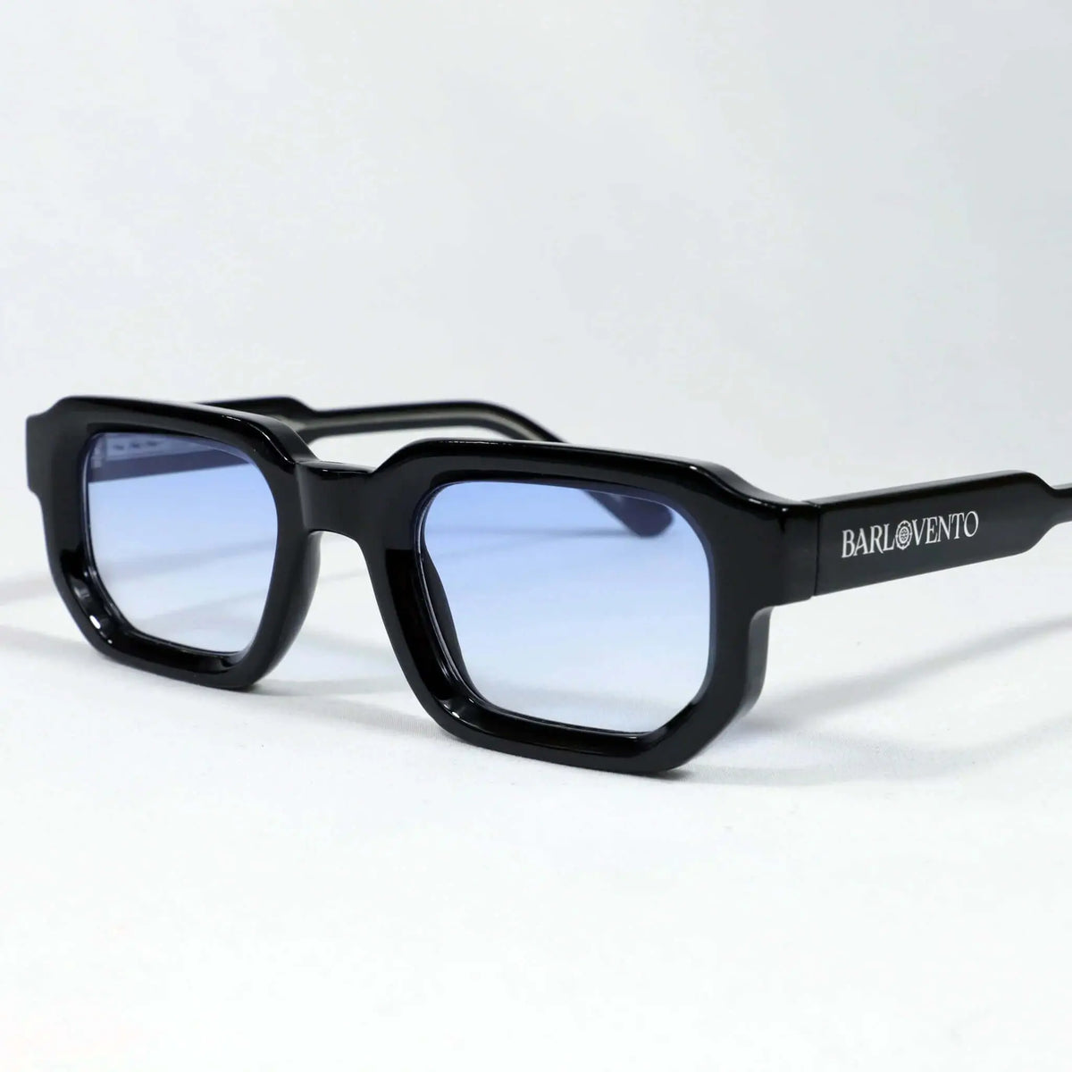 Gafas de sol rectangulares con marco grueso negro brillante y cristales tintados en azul claro.