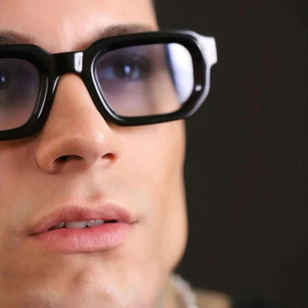 Gafas de sol con montura gruesa negra y lentes con degradado azul sobre una persona en primer plano.