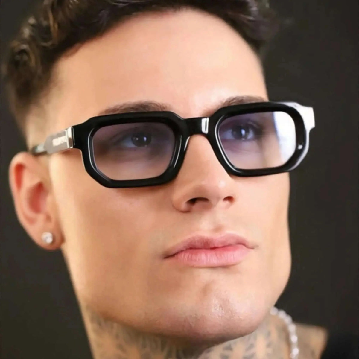 Gafas de sol con montura rectangular negra gruesa y lentes degradadas en tono azul claro sobre modelo masculino.