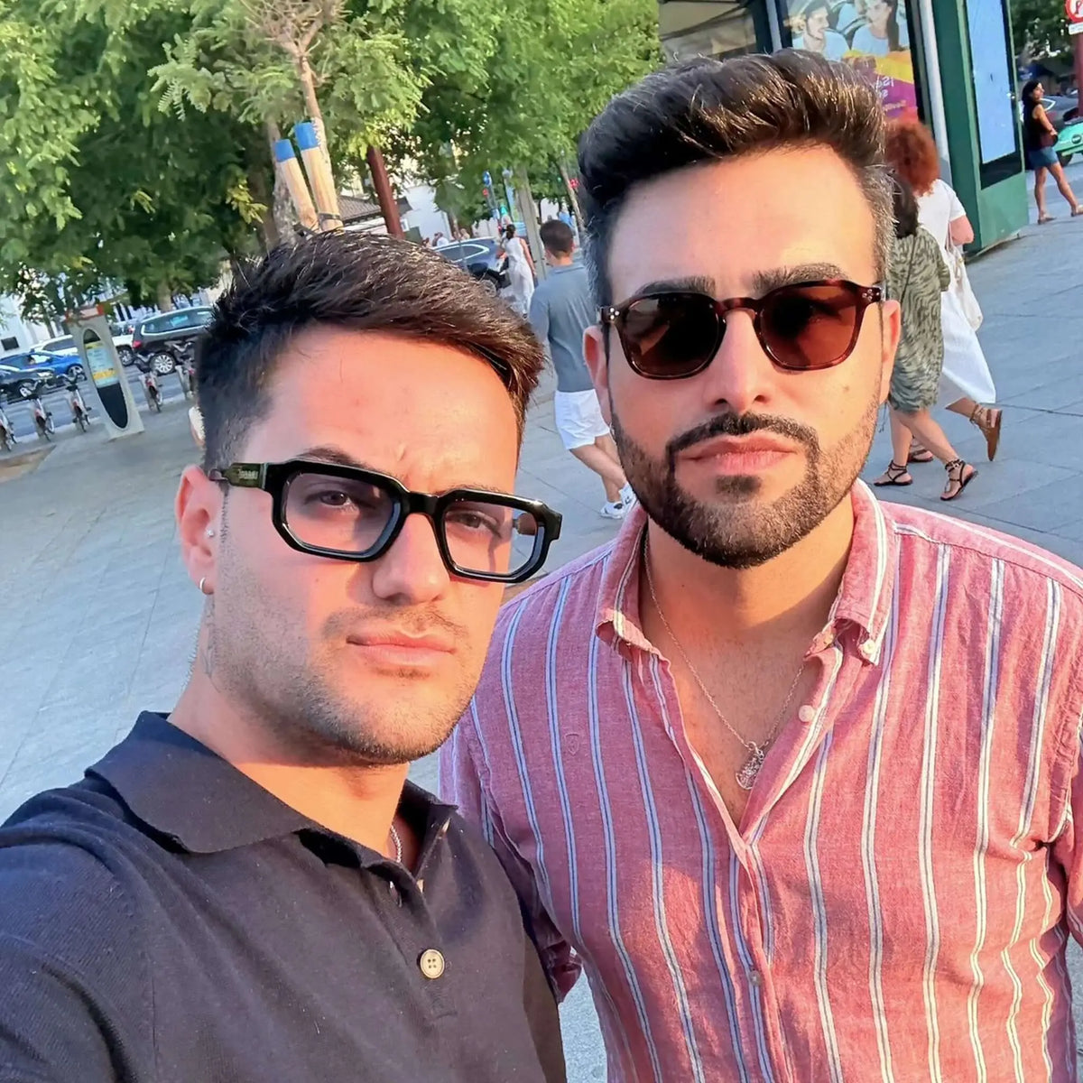 Gafas de sol con montura negra gruesa y lentes azuladas de estilo moderno y cuadrado.