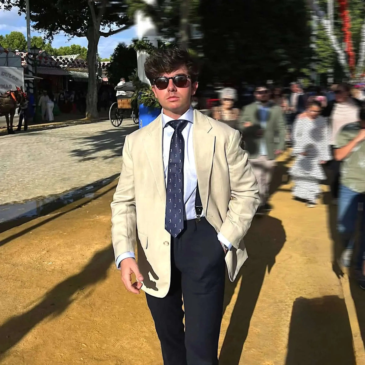 Hombre elegante con americana beige, camisa azul y corbata azul marino estampada con motivos de golf en feria al aire.