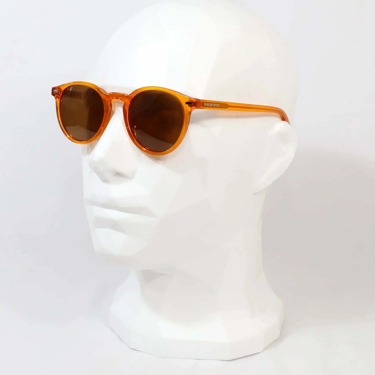 Gafas de sol unisex con montura redonda de acetato naranja transparente y cristales oscuros sobre maniquí blanco.