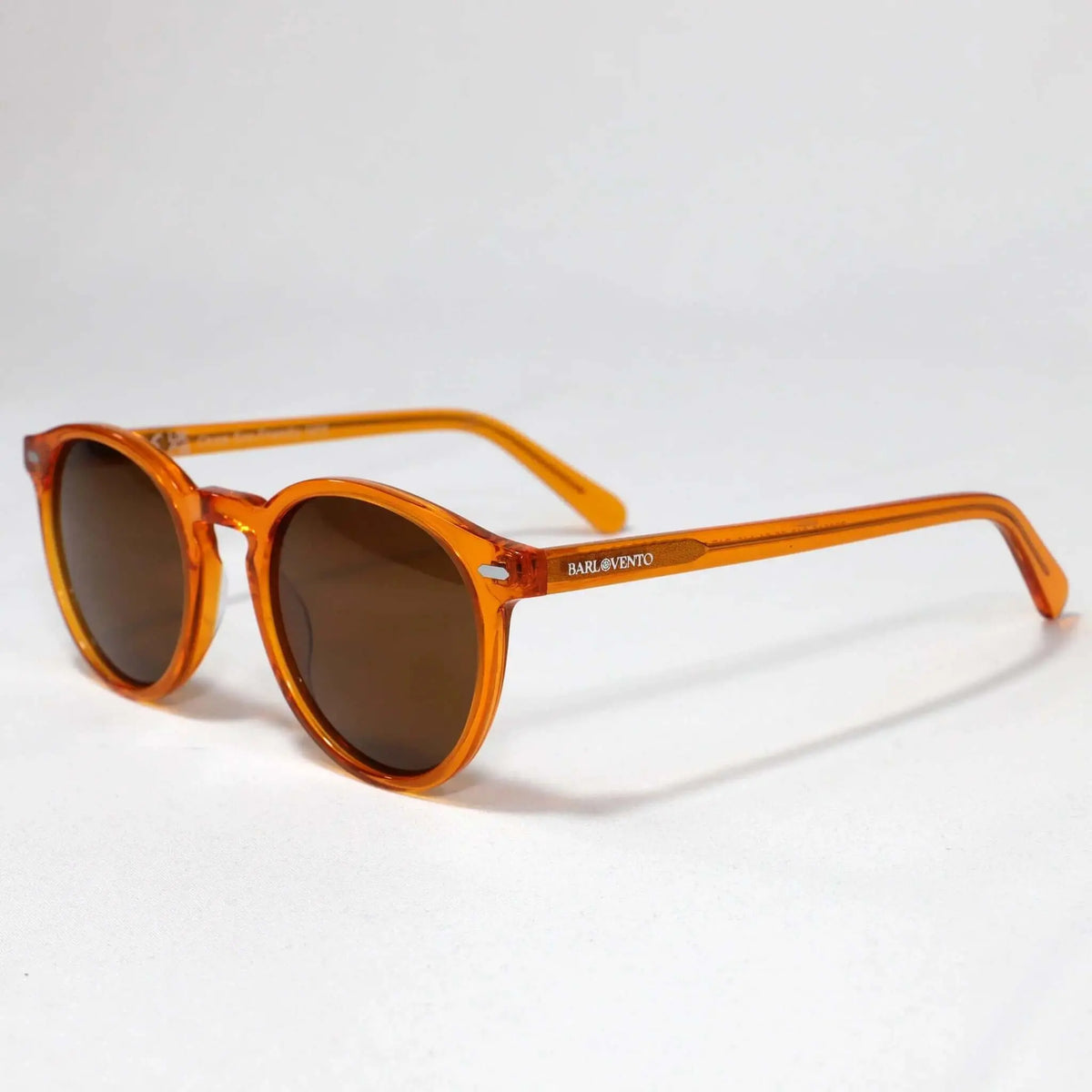 Gafas de sol redondas de acetato naranja transparente con cristales marrones oscuros sobre fondo blanco neutro.