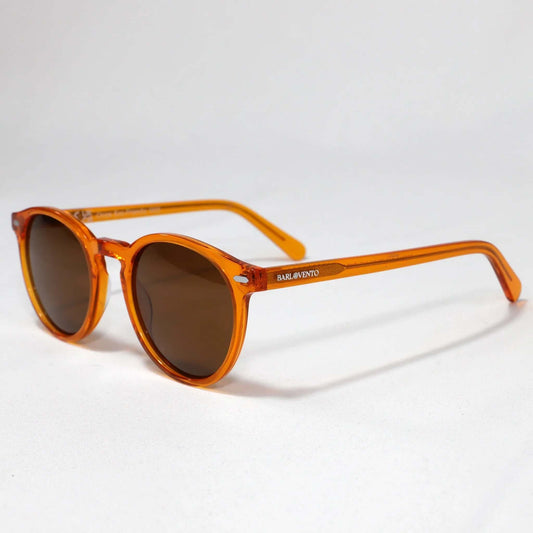 Gafas de sol redondas de acetato naranja transparente con cristales marrones oscuros sobre fondo blanco neutro.