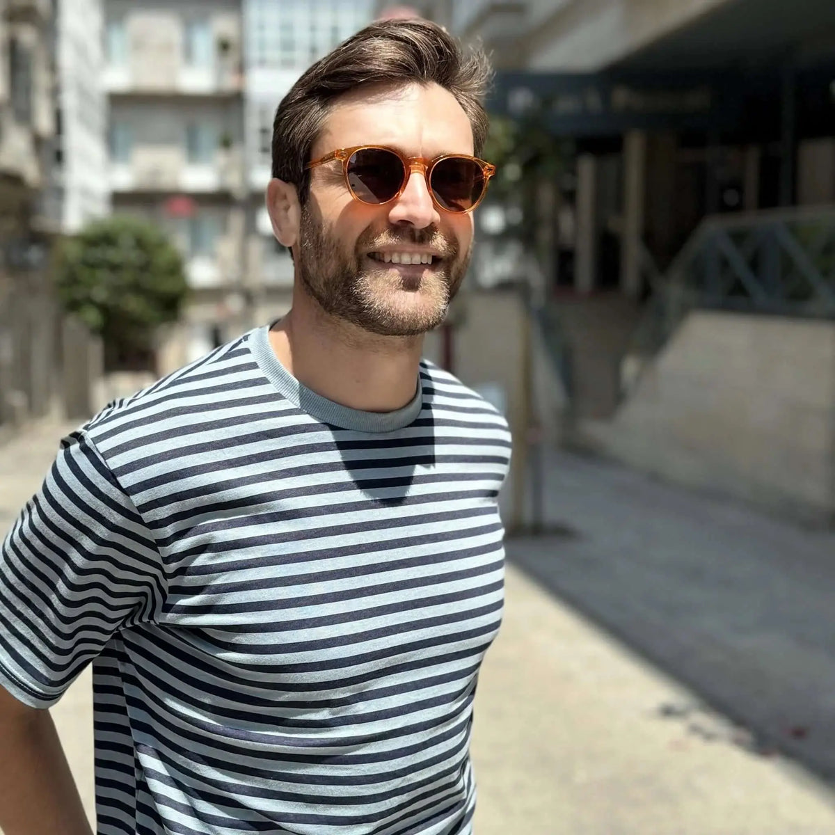 Hombre con gafas de sol redondas de acetato naranja transparente y camiseta de rayas, estilo urbano y casual.