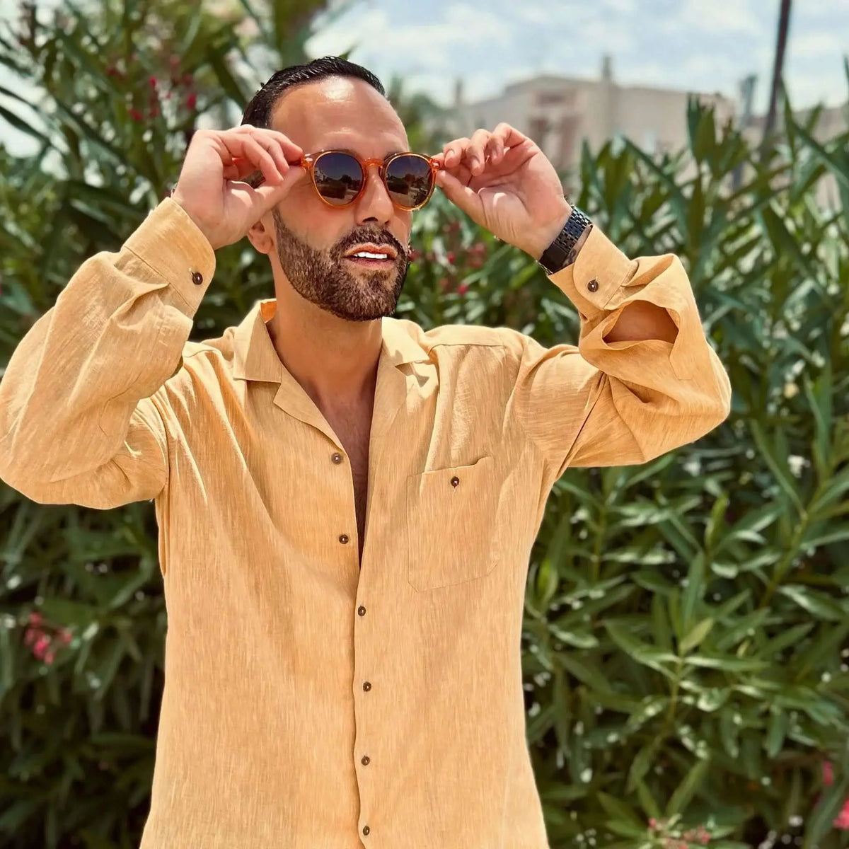 Hombre con camisa beige usando gafas de sol redondas de acetato naranja transparente estilo casual al aire libre.