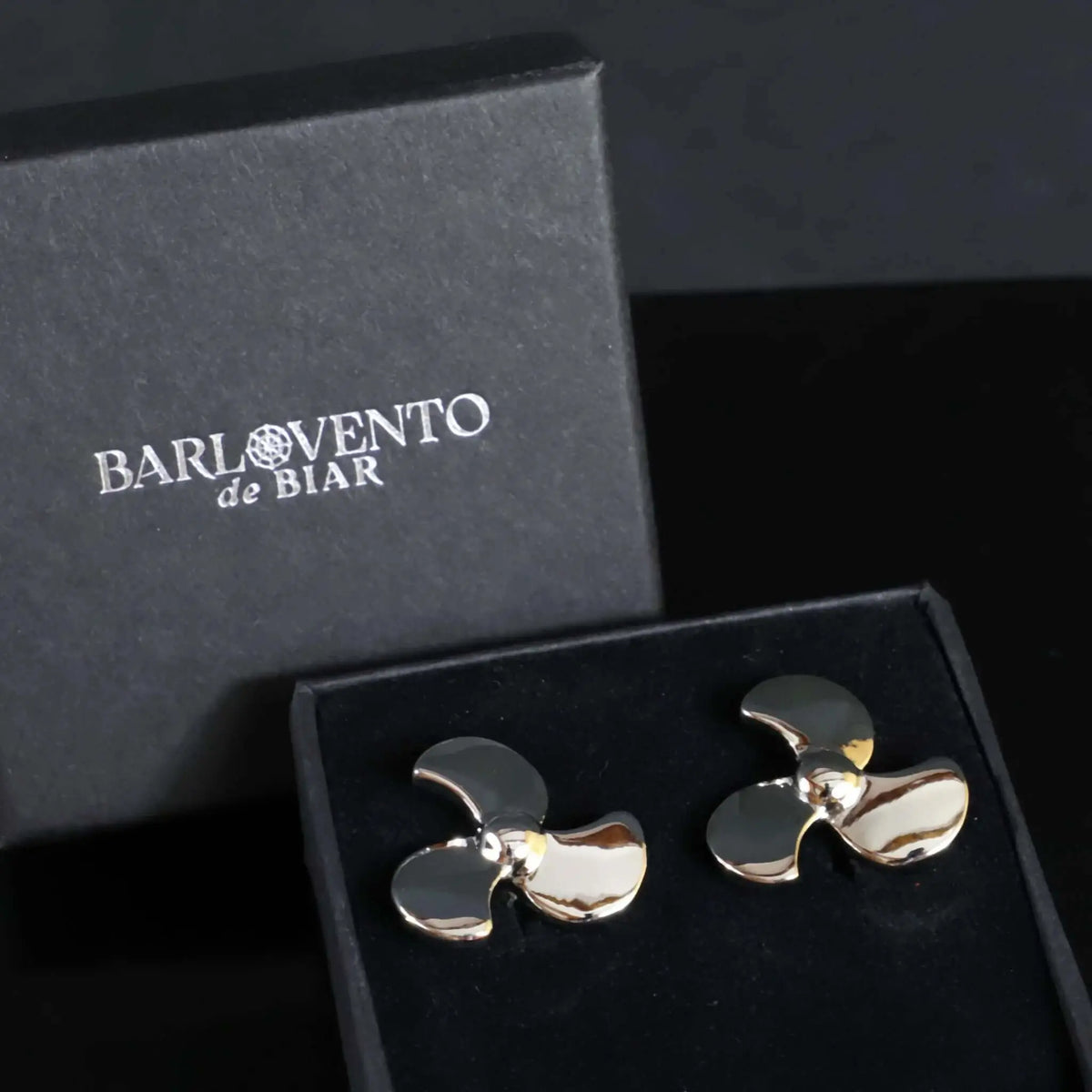 Gemelos de camisa plateados con forma de hélice de barco, acabado pulido brillante, presentados en caja de regalo negra.