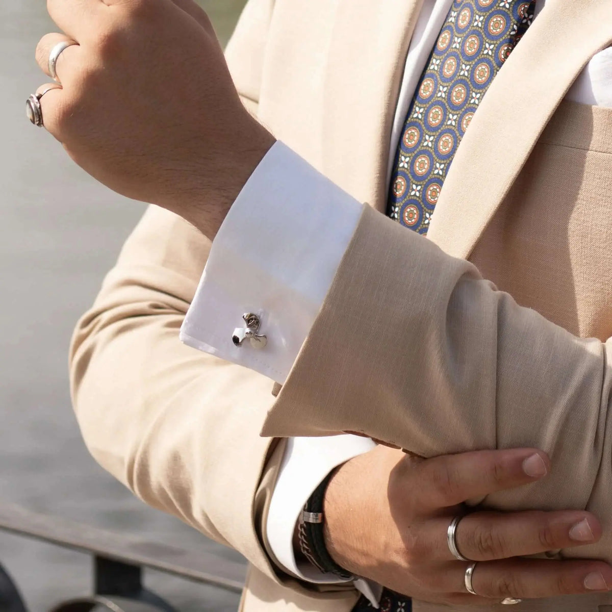 Gemelos de camisa plateados con forma de hélice de barco en puño blanco y traje beige. Estilo náutico elegante.