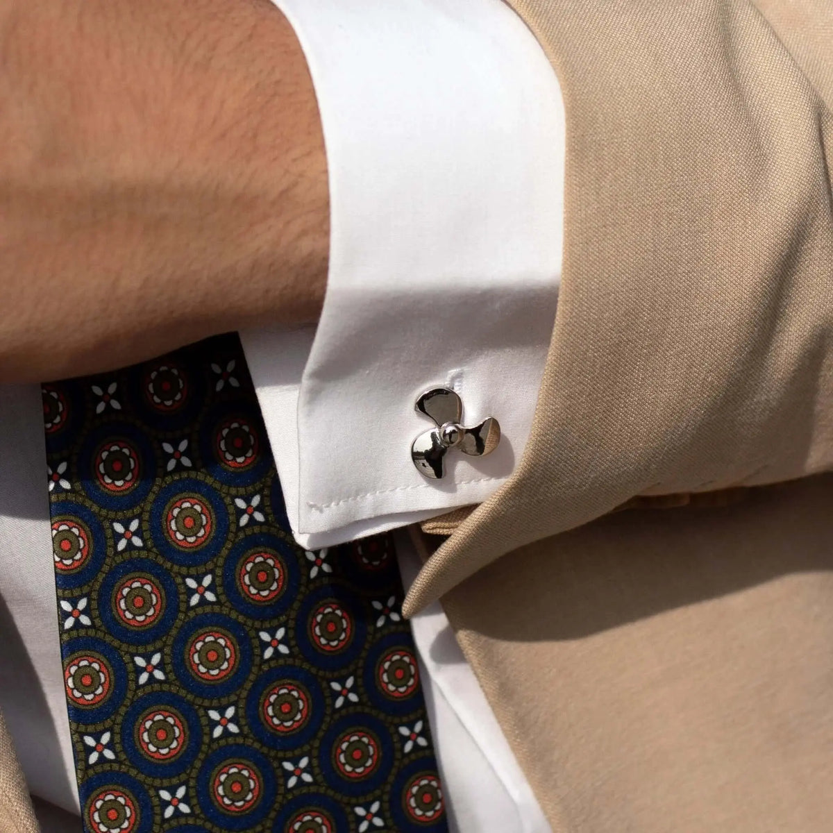Gemelos de camisa con forma de hélice de barco en metal plateado brillante sobre puño blanco y americana beige.