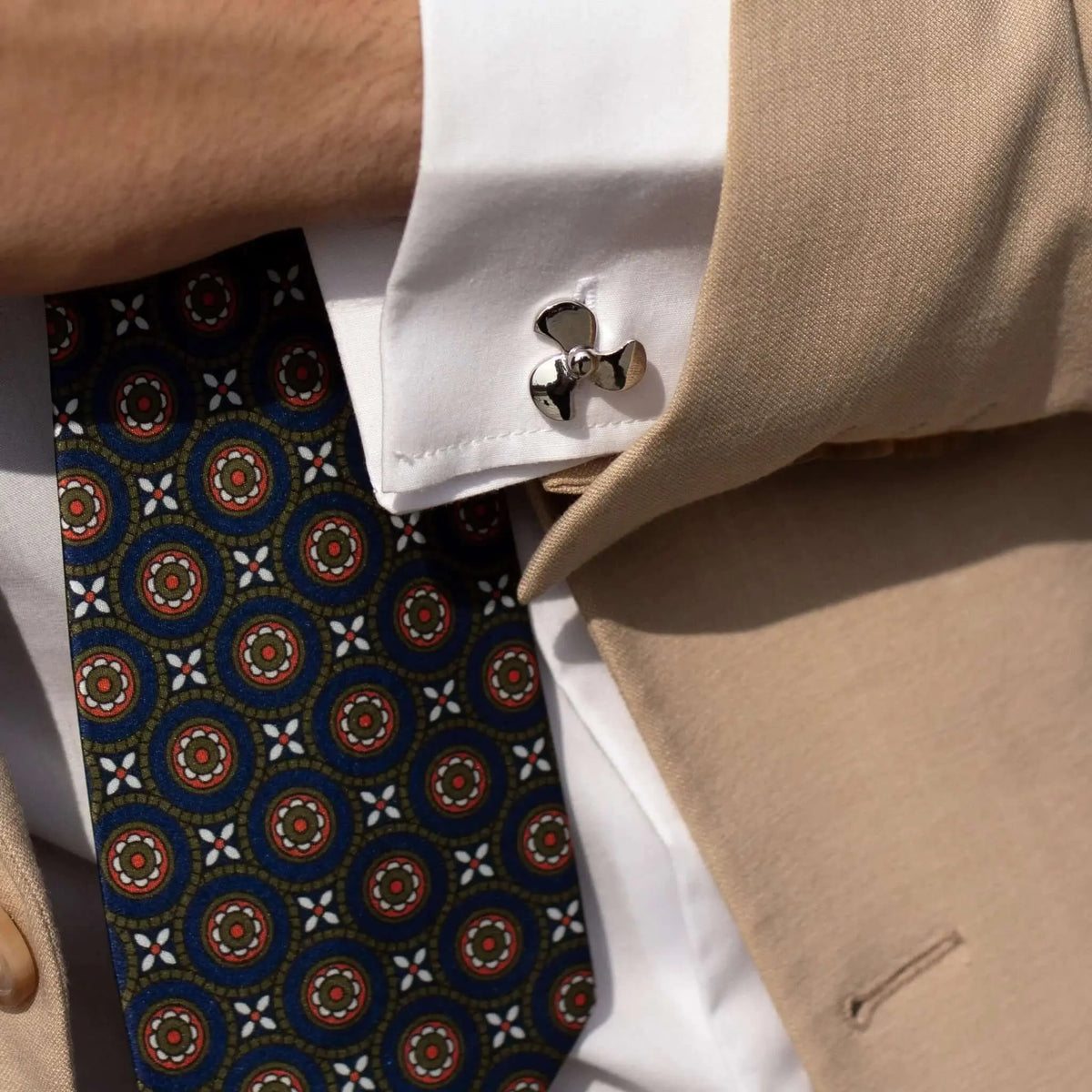 Gemelos plateados con forma de hélice de barco en puño de camisa blanca, estilo náutico elegante y moderno.