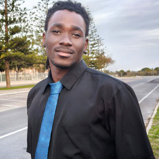 Hombre luciendo un conjunto de corbata azul con estampado de hojas, pañuelo, gemelos y pasador.