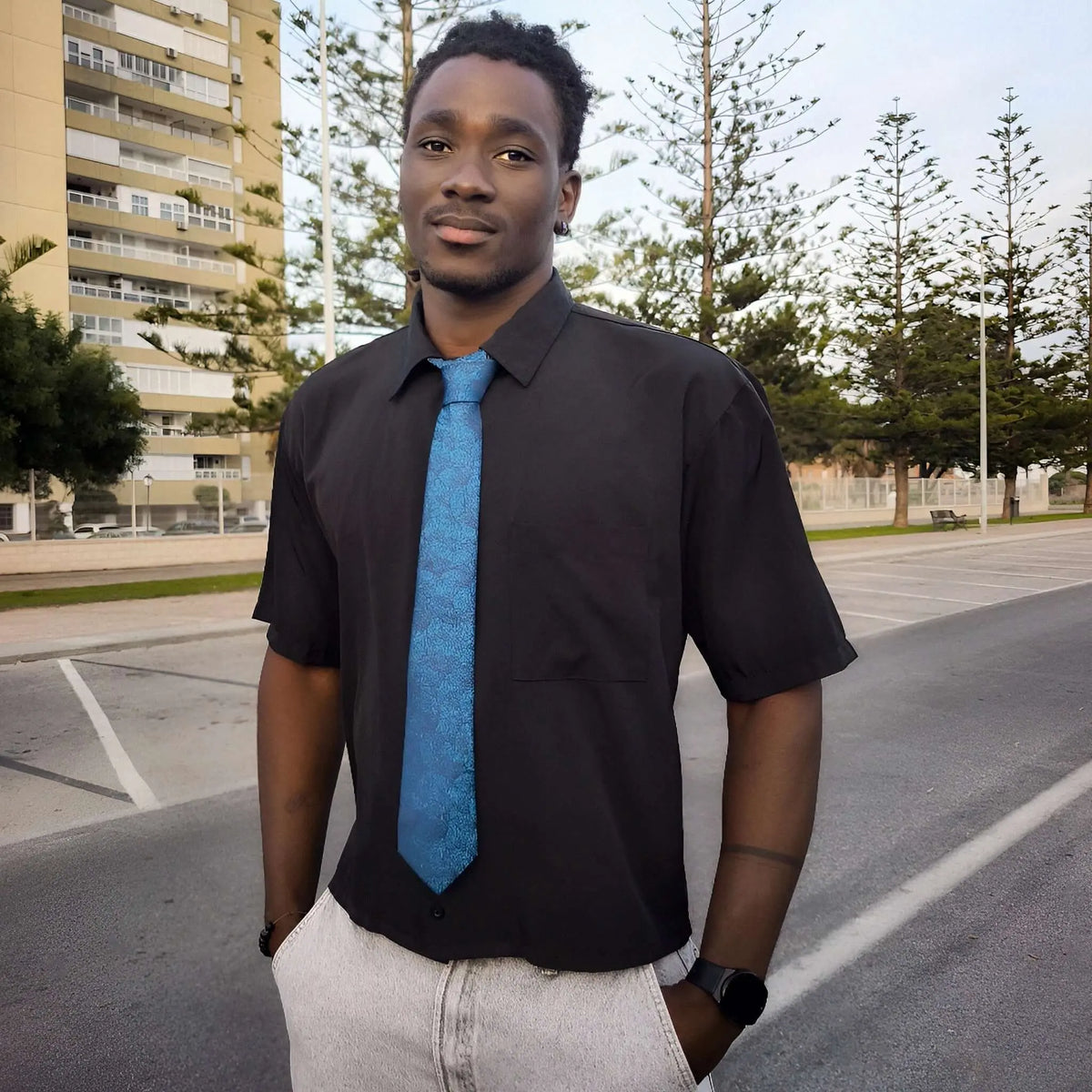 Hombre con camisa negra y corbata azul con estampado de hojas, estilo elegante y natural en exteriores.