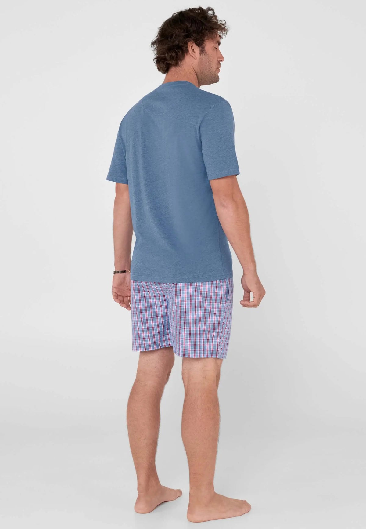 Hombre con pijama corto: camiseta azul lisa y pantalón de cuadros azules y rojos. Vista trasera.