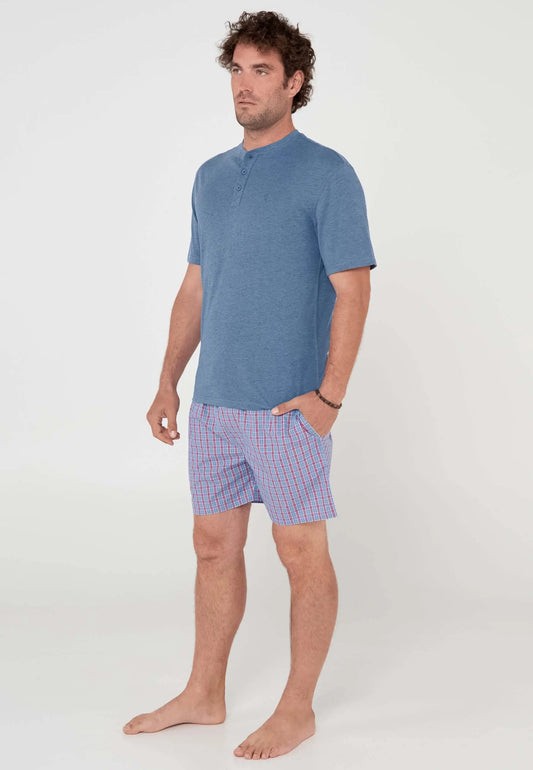 Modelo con pijama corto de camiseta azul lisa con botones y pantalón de cuadros azules y rojos.