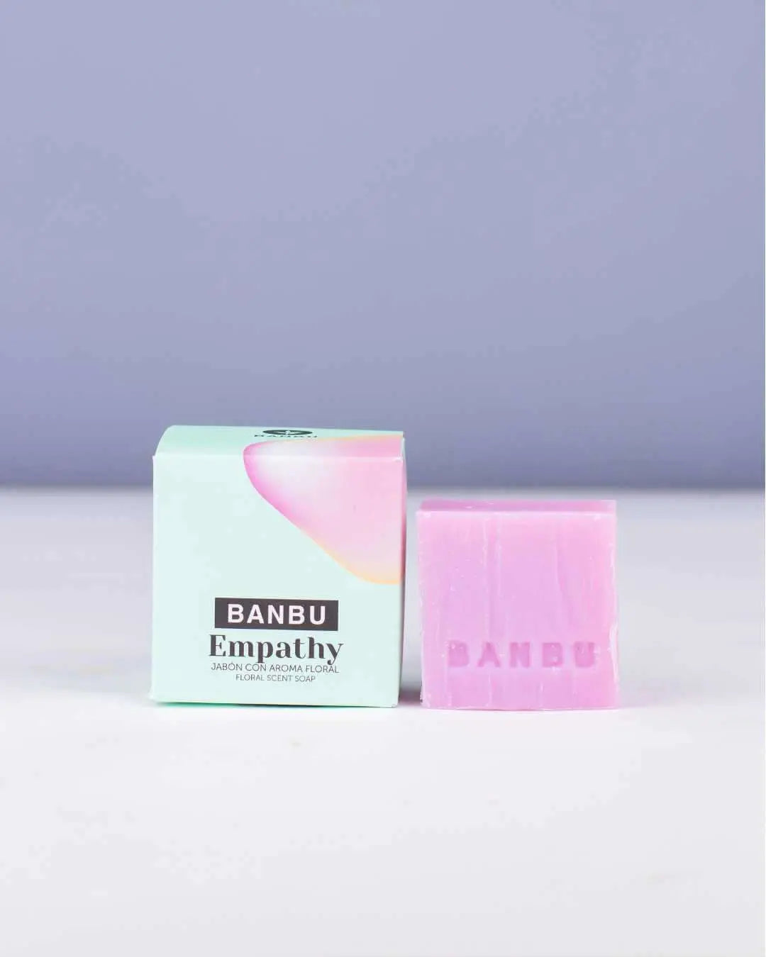 Jabón sólido rosa Banbu Empathy junto a su caja de cartón verde claro sobre fondo lila. Diseño minimalista y natural.