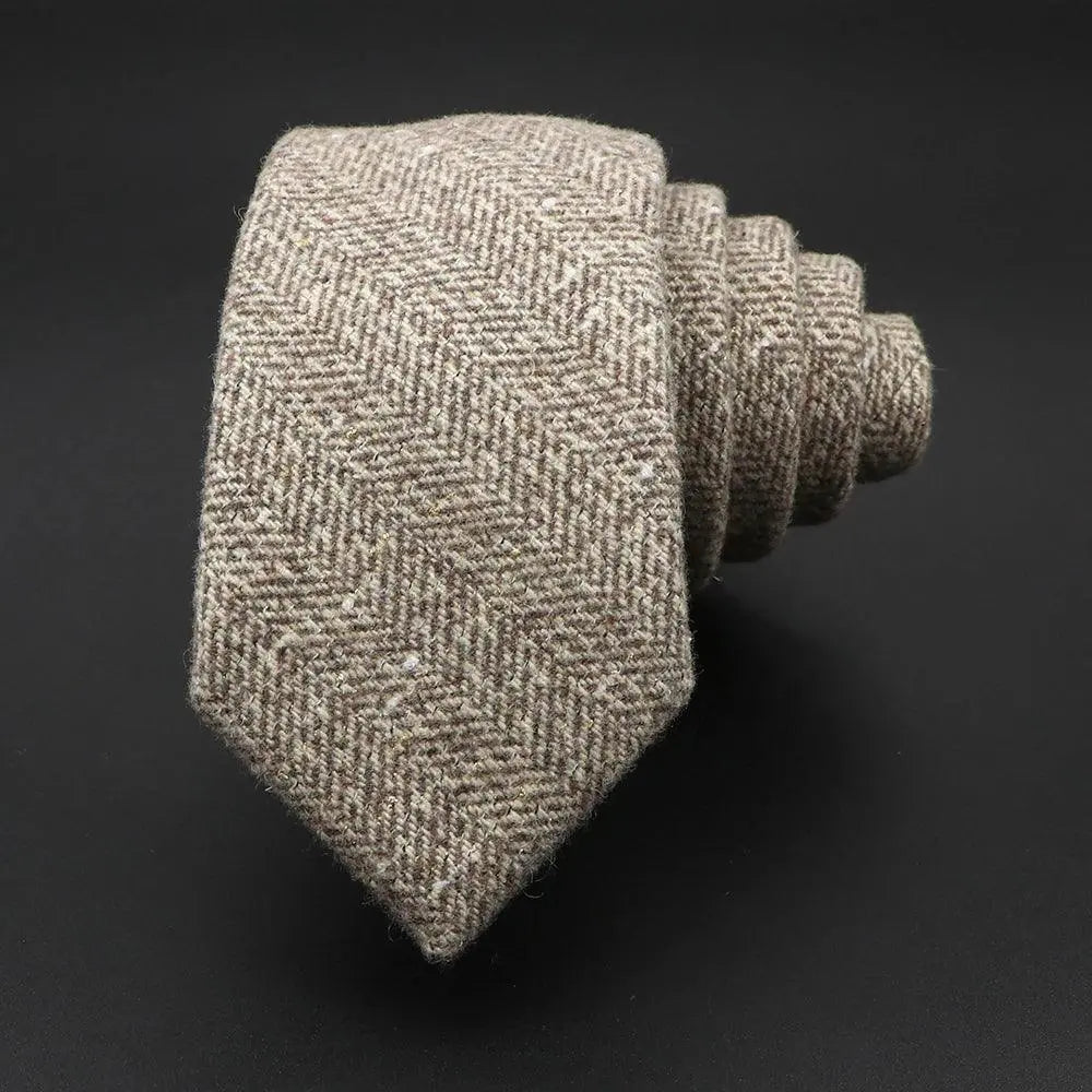 Corbata de lana en color beige con patrón de espiga y textura rústica, enrollada sobre fondo negro.