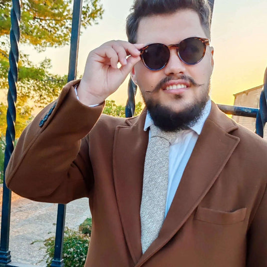 Hombre con americana marrón y corbata de lana beige con textura de espiga, estilo elegante al aire libre.