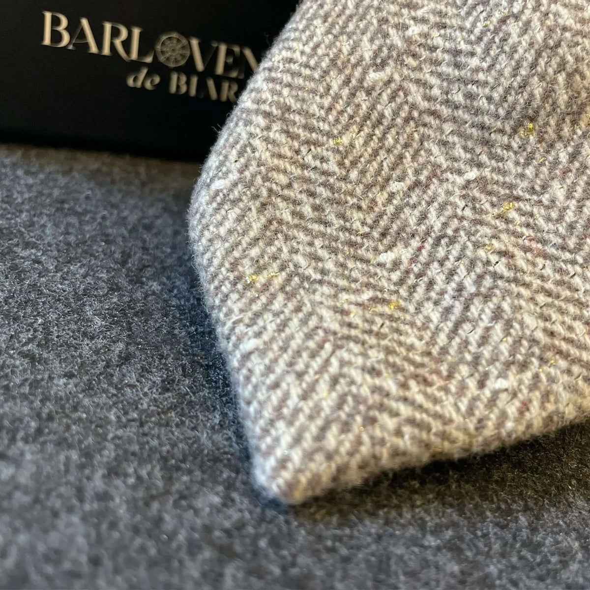 Corbata de lana beige con patrón de espiga y sutiles destellos dorados, textura artesanal y estilo clásico.