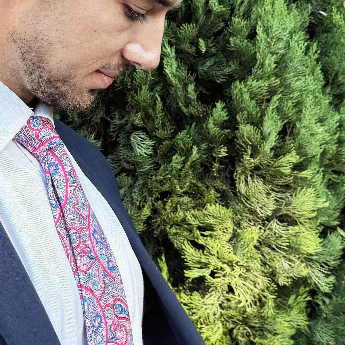 Corbata con estampado paisley en tonos rosa, azul y blanco sobre camisa blanca y traje azul marino.