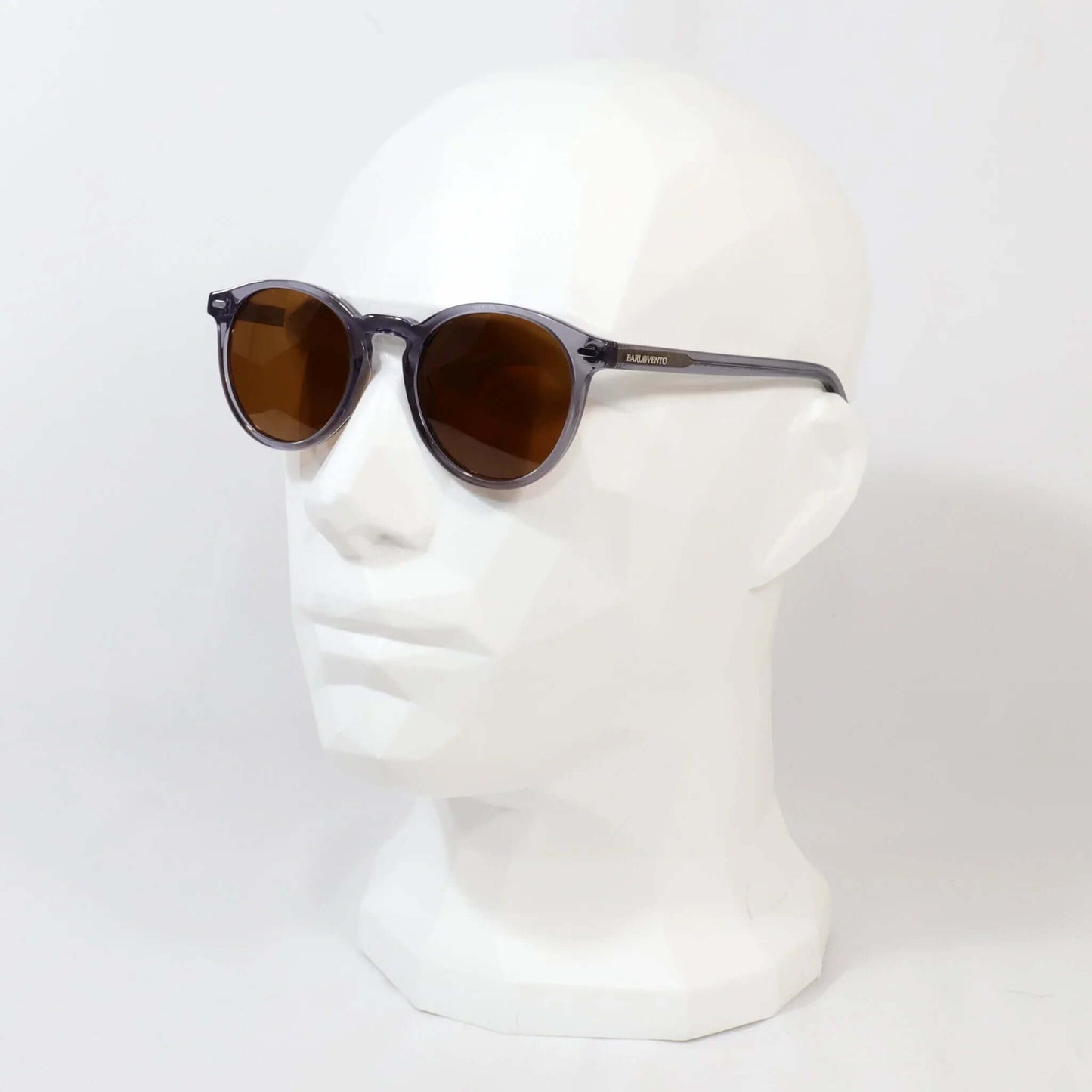 Gafas de sol redondas con montura de acetato gris cristal transparente y lentes oscuras sobre un maniquí blanco.