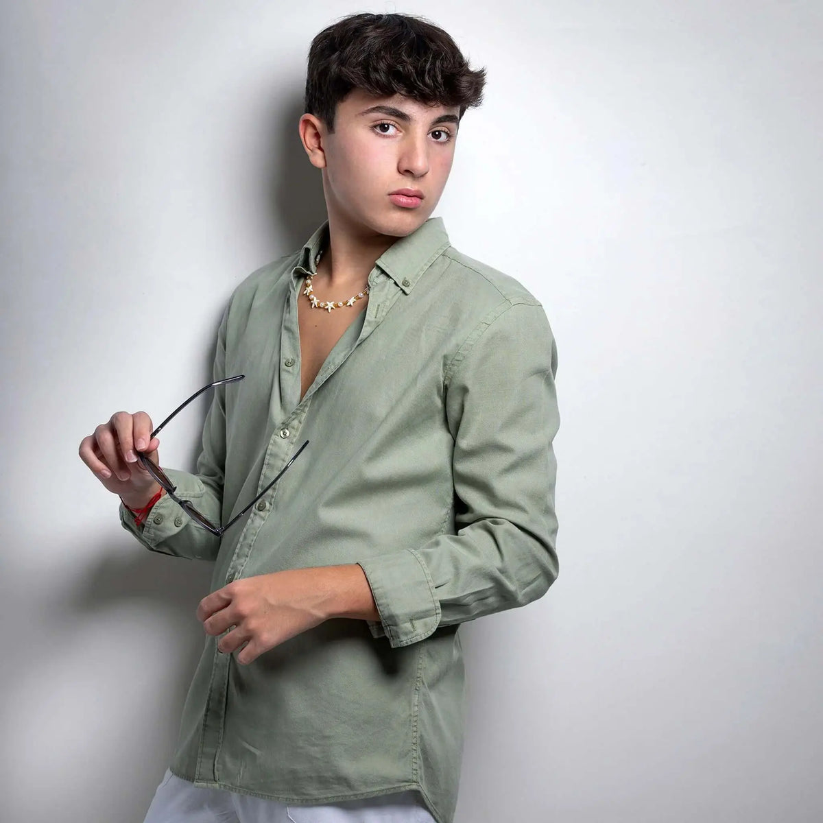 Joven con camisa verde y gafas de sol redondas de acetato gris cristal, estilo casual y moderno sobre fondo neutro.