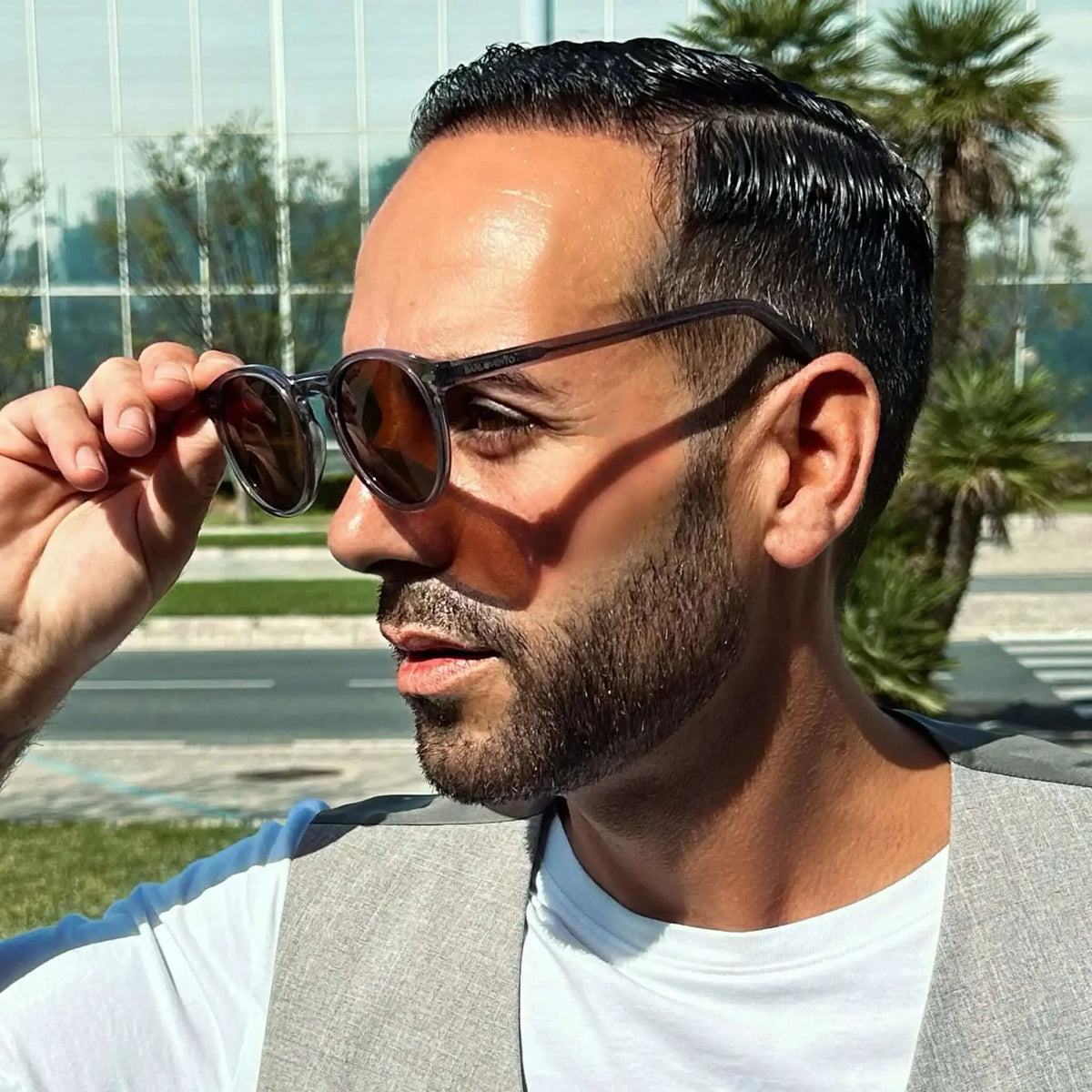 Hombre con gafas de sol redondas de montura gris cristal translúcido, estilo casual al aire libre.