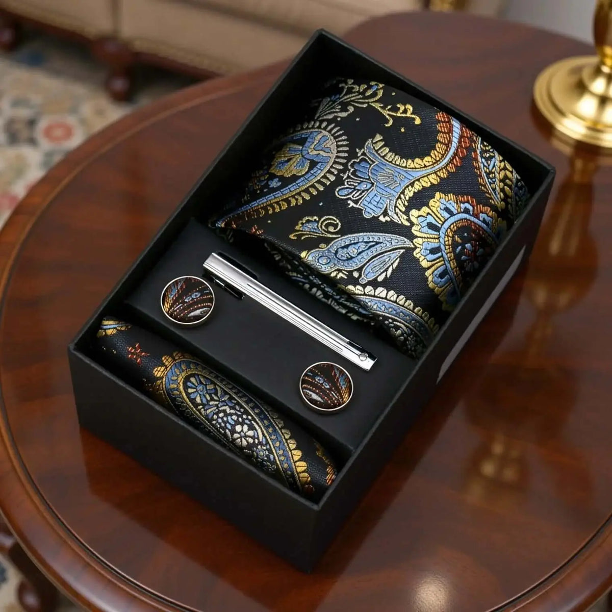 Set de regalo: corbata de seda con estampado paisley azul y dorado, pañuelo, gemelos y pisacorbata en caja negra.