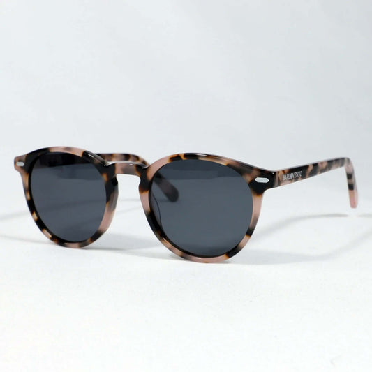 Gafas de sol redondas con montura de acrílico estampado carey en tonos marrones y cristales oscuros sobre fondo blanco.
