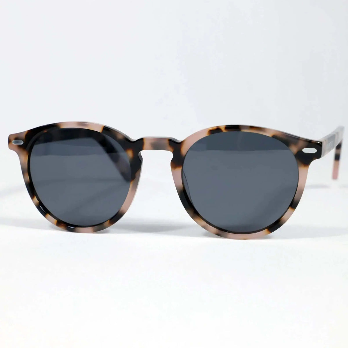 Gafas de sol redondas con montura de acrílico estampado carey en tonos marrones y cristales oscuros sobre fondo blanco.