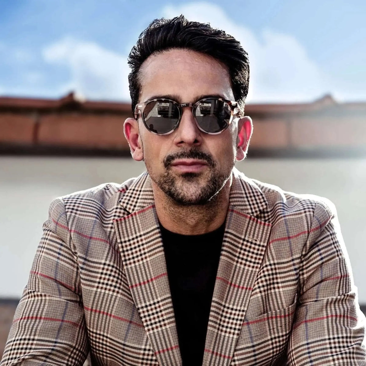 Hombre con gafas de sol redondas de carey y chaqueta de cuadros estilo elegante al aire libre.