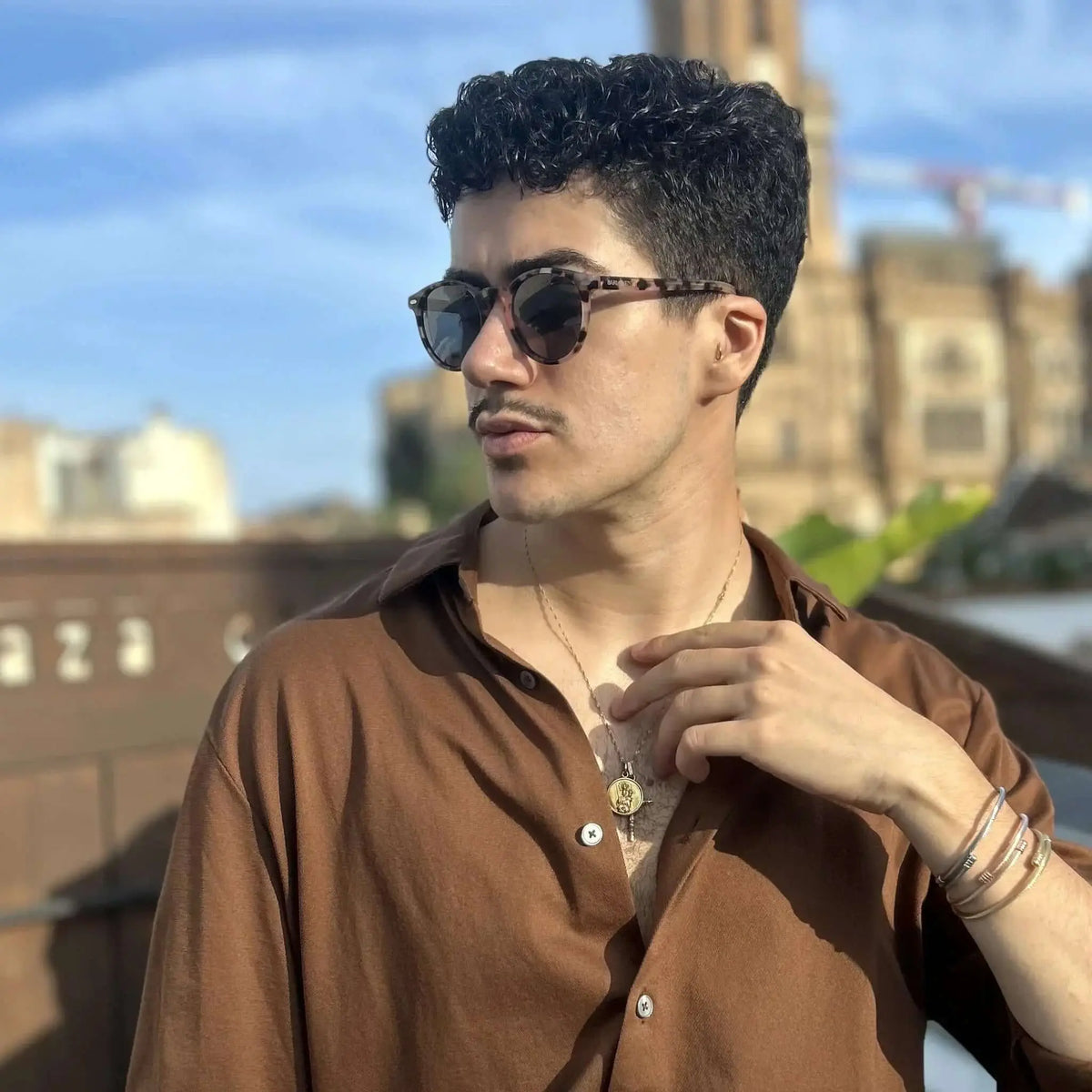 Joven con camisa marrón y gafas de sol redondas de acrílico con estampado de carey y acabado brillante en exterior.
