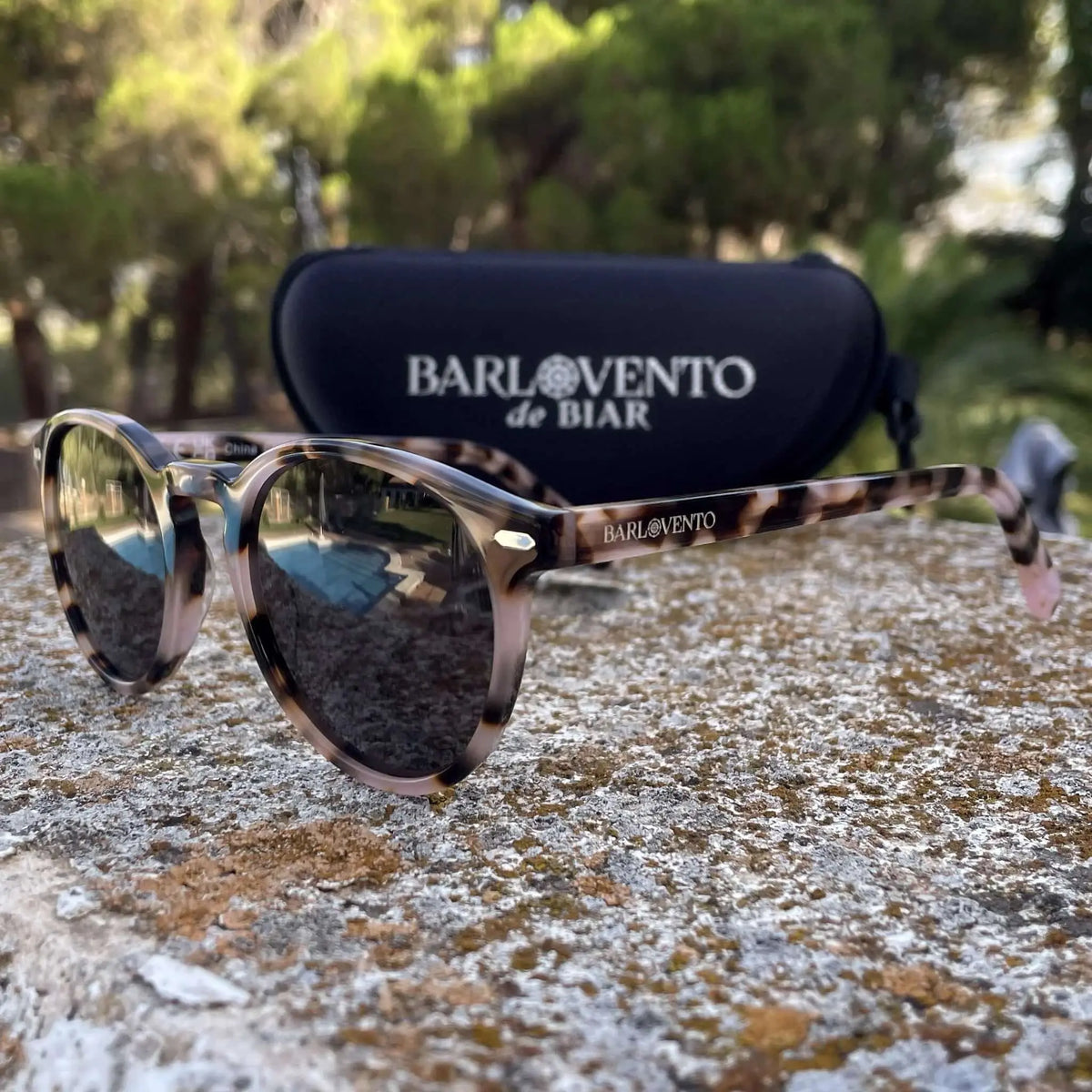 Gafas de sol redondas con montura de acrílico estampado carey en tonos marrones y beige sobre superficie de piedra.