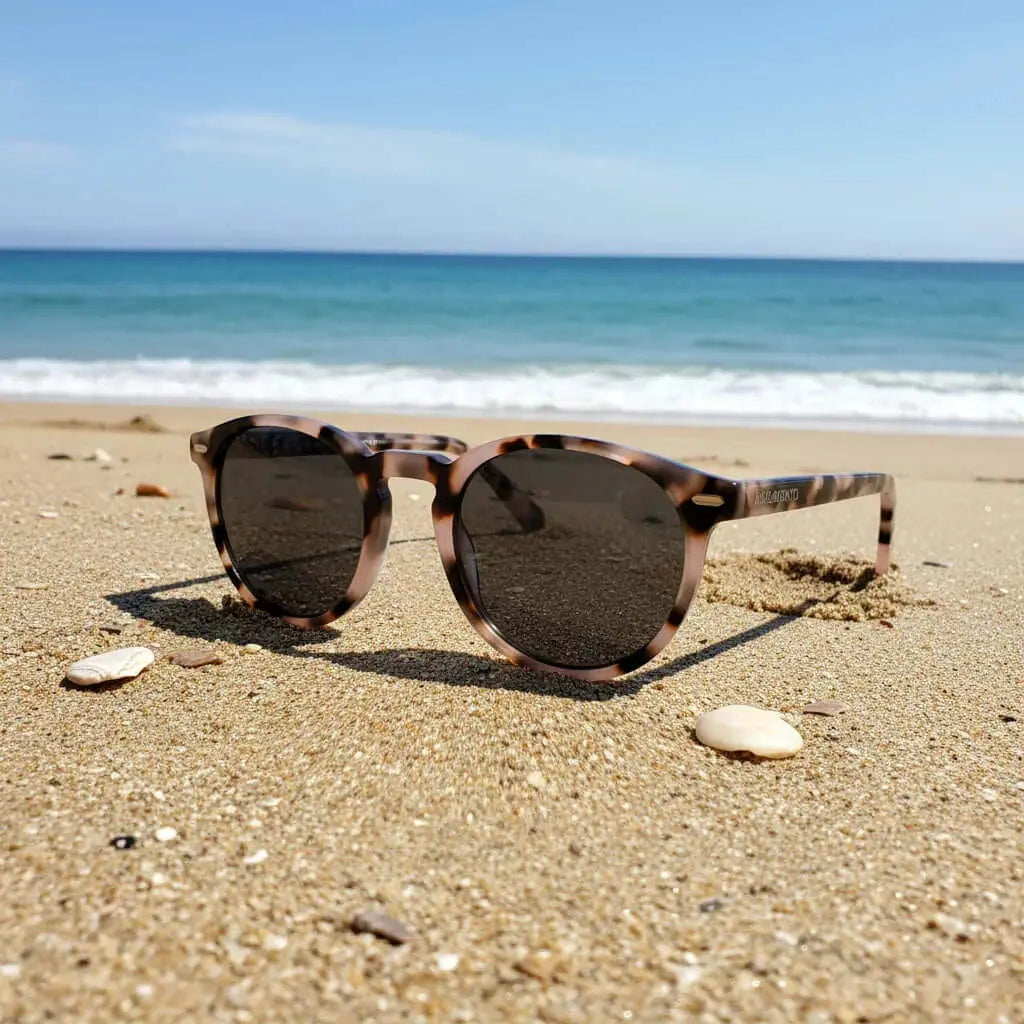 Gafas de sol redondas con montura de acrílico efecto carey y cristales oscuros sobre la arena en la playa.