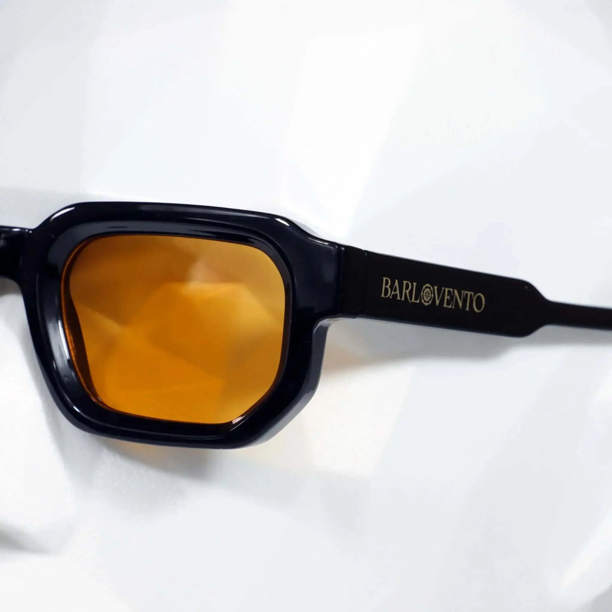 Gafas de sol negras de estilo rectangular con montura gruesa y lentes naranjas brillantes. Diseño moderno y elegante.
