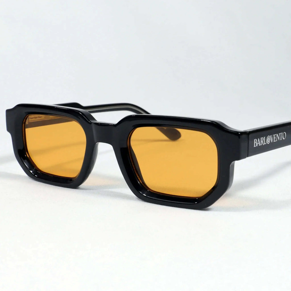 Gafas de sol rectangulares con montura negra brillante y lentes color naranja, estilo moderno y audaz sobre fondo blanco.