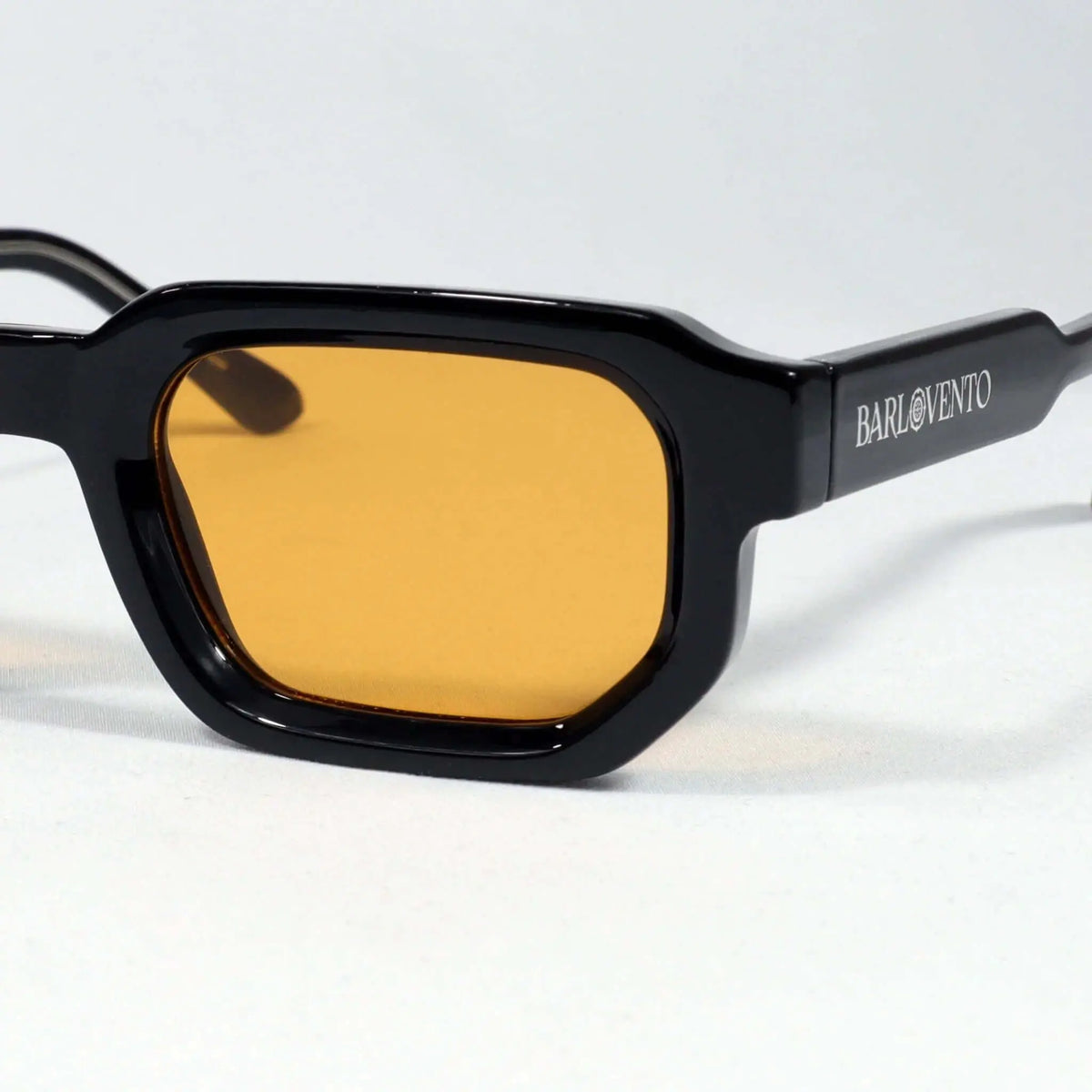 Gafas de sol negras de estilo moderno con montura gruesa rectangular y lentes color naranja intenso sobre fondo blanco.