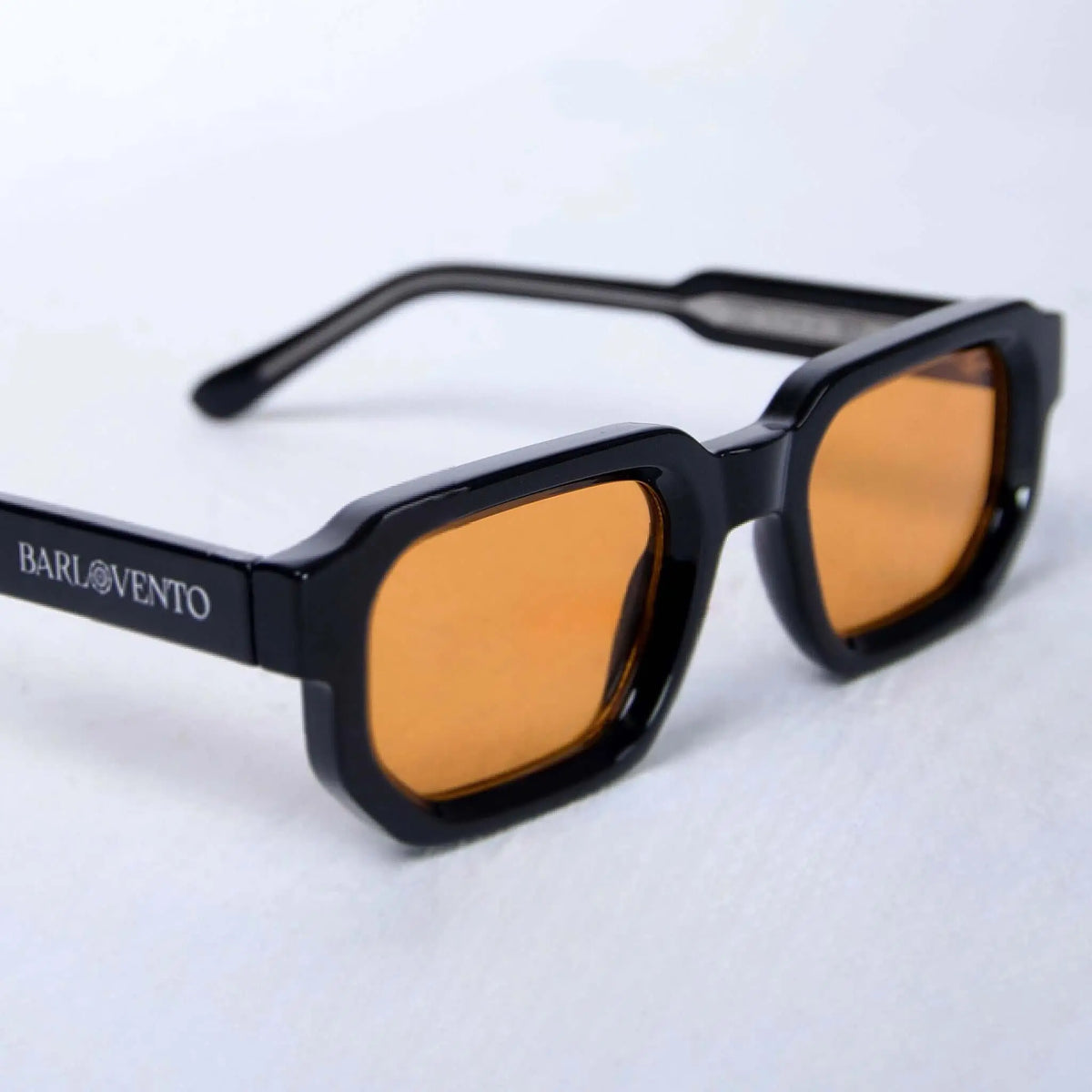 Gafas de sol de montura negra cuadrada con acabado brillante y lentes naranjas, estilo moderno sobre fondo blanco.