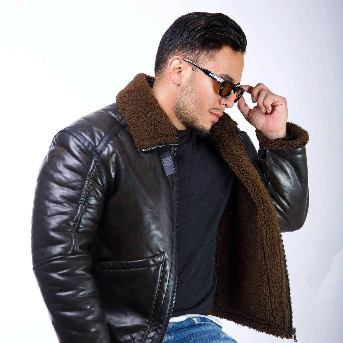 Hombre con chaqueta de cuero y gafas de sol de marco negro con lentes naranjas en estudio sobre fondo blanco.