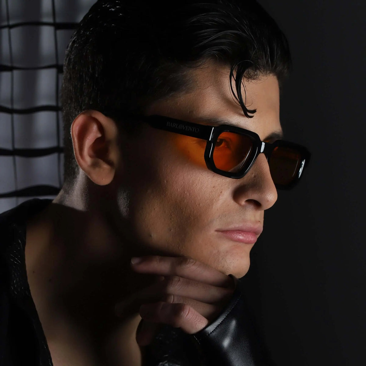 Hombre con gafas de sol negras de montura gruesa rectangular y lentes naranjas, estilo moderno y elegante.