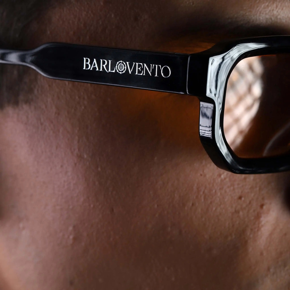 Gafas de sol negras de estilo geométrico con lentes color naranja puestas en primer plano sobre un rostro masculino.
