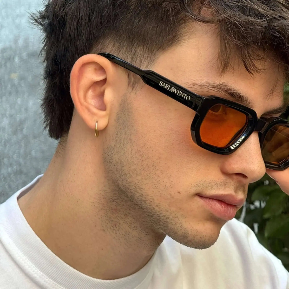 Hombre joven con gafas de sol negras de montura rectangular y lentes naranjas, estilo moderno en primer plano.