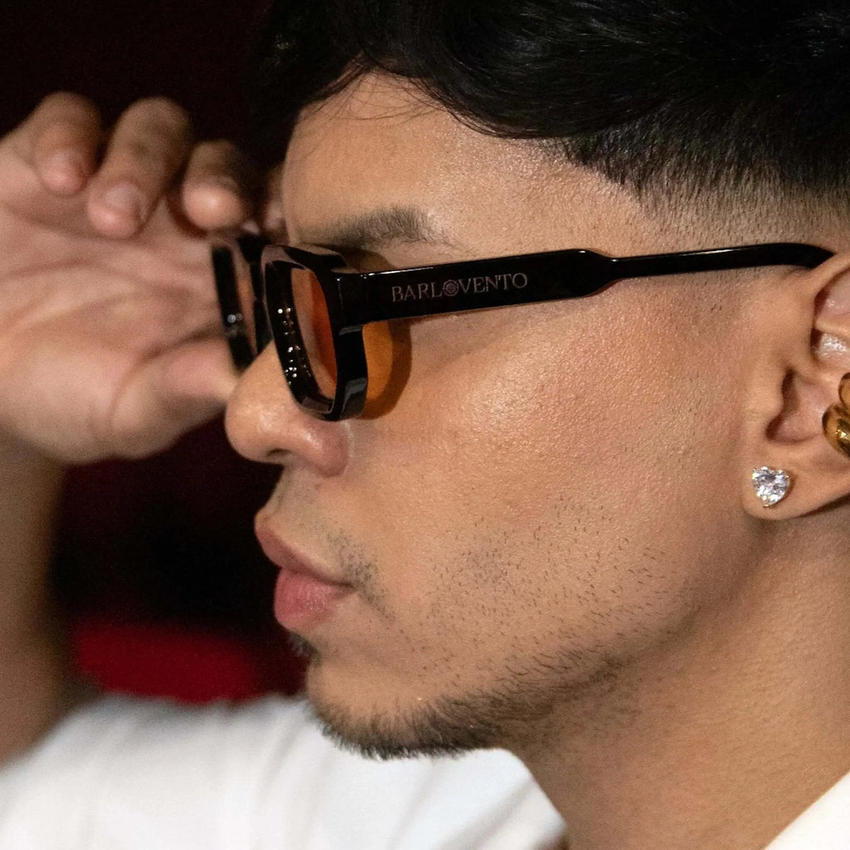 Hombre con gafas de sol negras de montura gruesa y lentes naranjas, estilo moderno en primer plano.